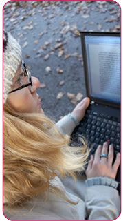 A young woman in a woolly hat and jumper using her laptop in the park